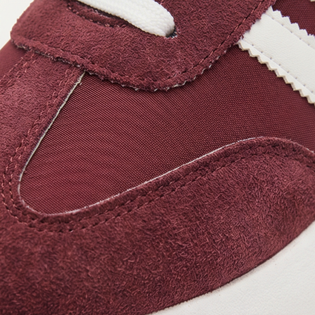 Close up of a burgundy suede sneaker toe with white side stripes and a textured panel