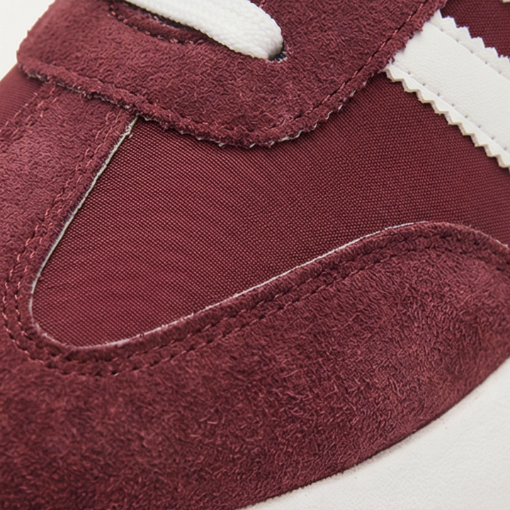 Close up of a burgundy suede sneaker toe with white side stripes and a textured panel