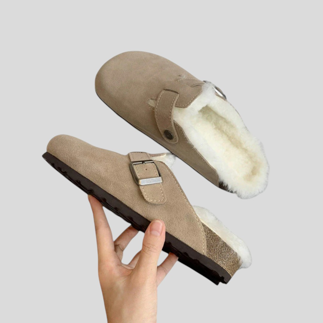 Pair of taupe suede clogs with a buckle strap and cream shearling lining, held up
