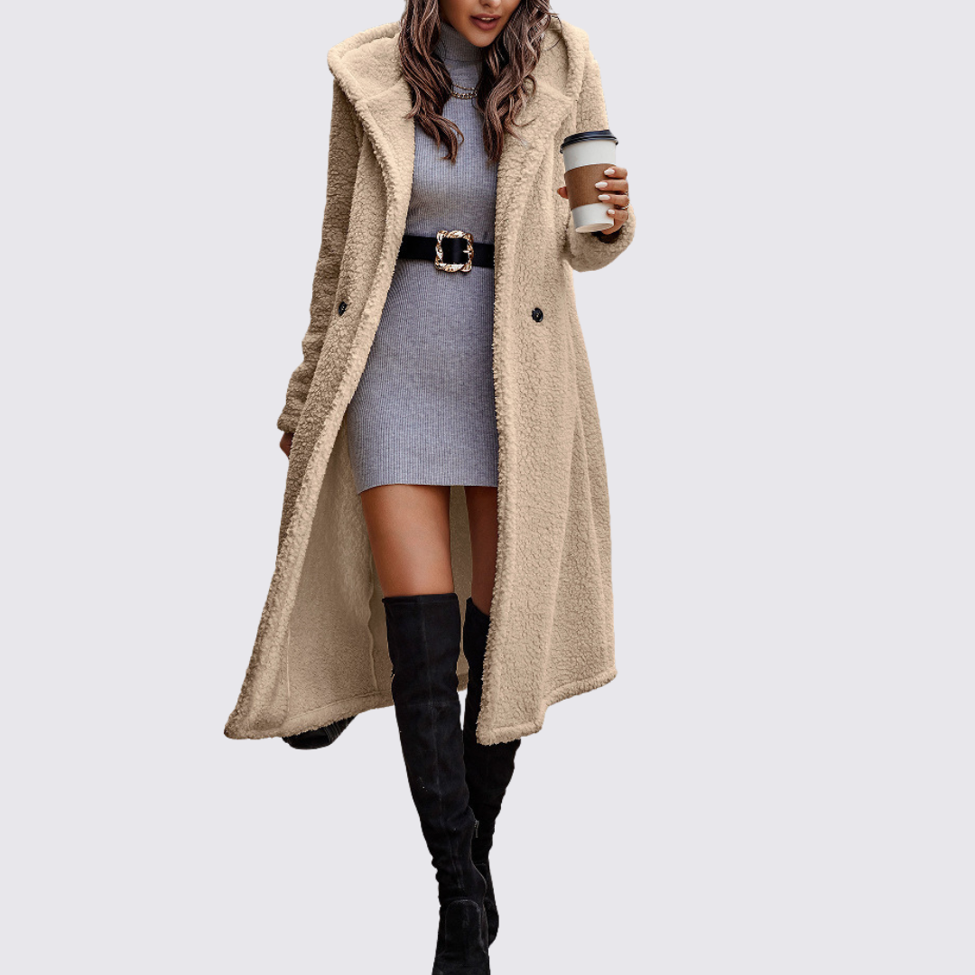 Woman wearing a long cream teddy fleece coat with a hood and button front, styled over a grey dress