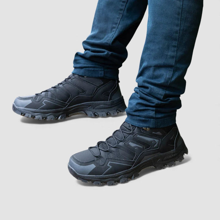 Pair of black lace up hiking shoes with grey panels and deep tread, worn with jeans