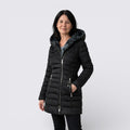 Woman wearing a black quilted jacket with a grey faux fur lined hood and silver zip pockets, front view