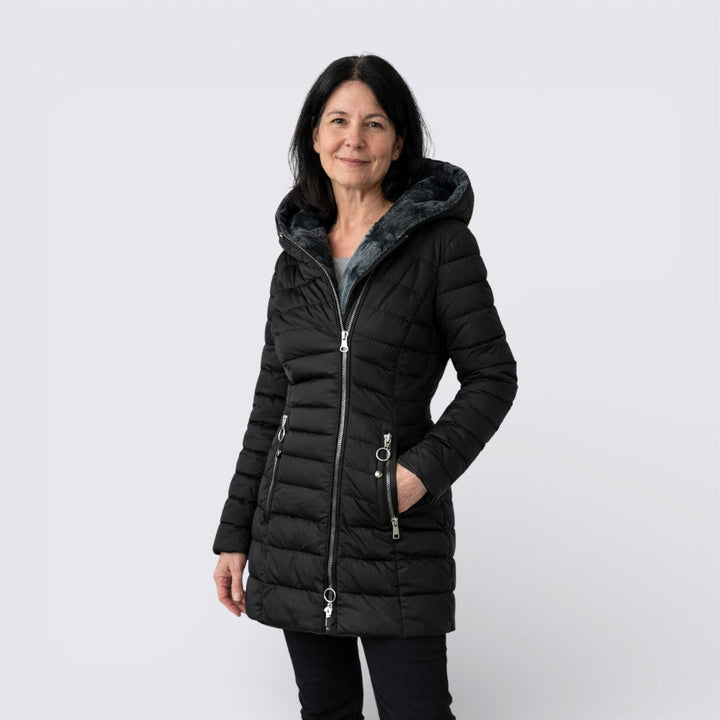 Woman wearing a black quilted jacket with a grey faux fur lined hood and silver zip pockets, front view