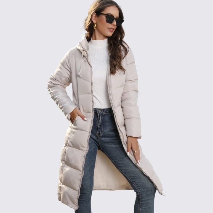 Woman in a beige long quilted hooded puffer coat worn open over jeans and a white top