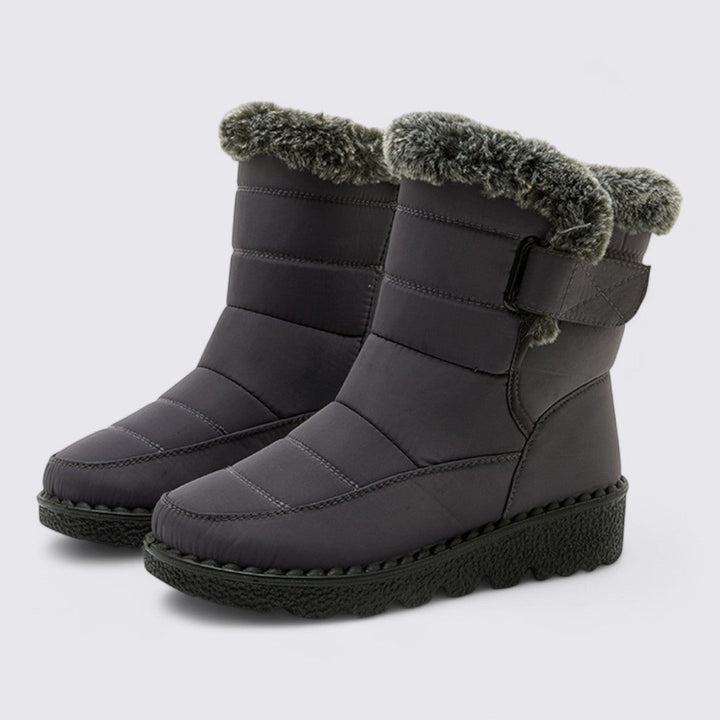 Pair of dark grey padded snow boots with faux fur lined cuffs and thick treaded soles, angled view