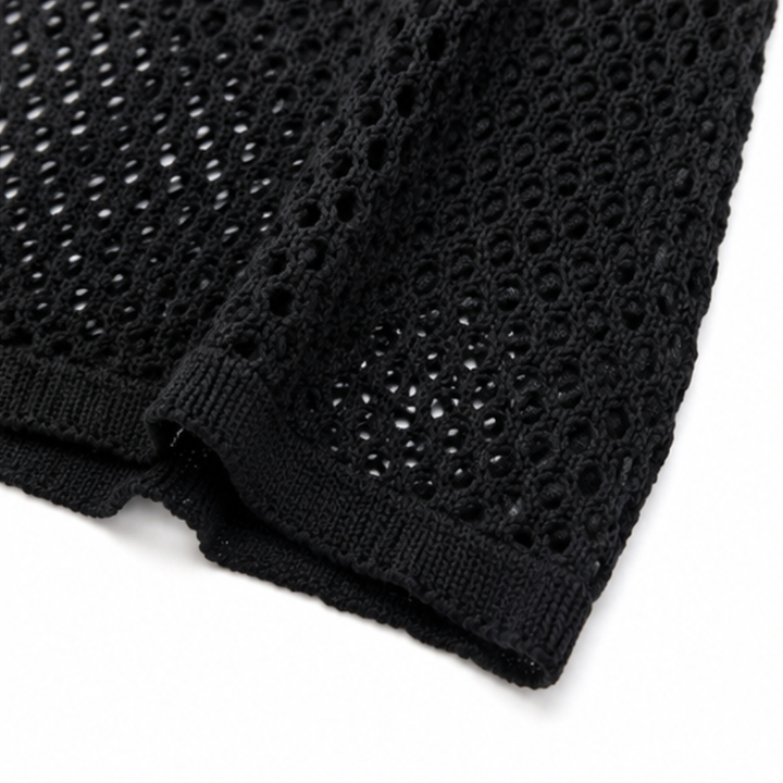 Close up of the black open knit fabric and ribbed hem of a cardigan