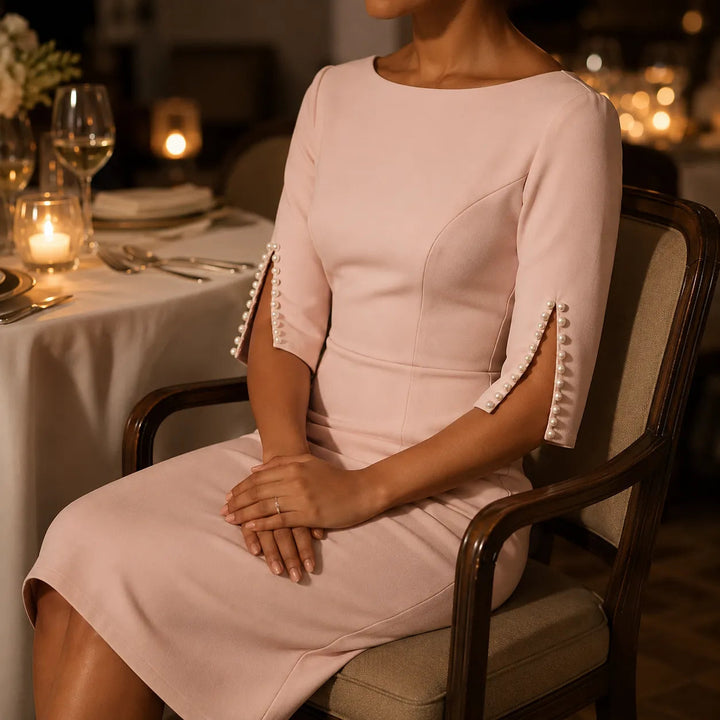 Woman seated at a candlelit table in a blush pencil dress with pearl trimmed sleeve openings