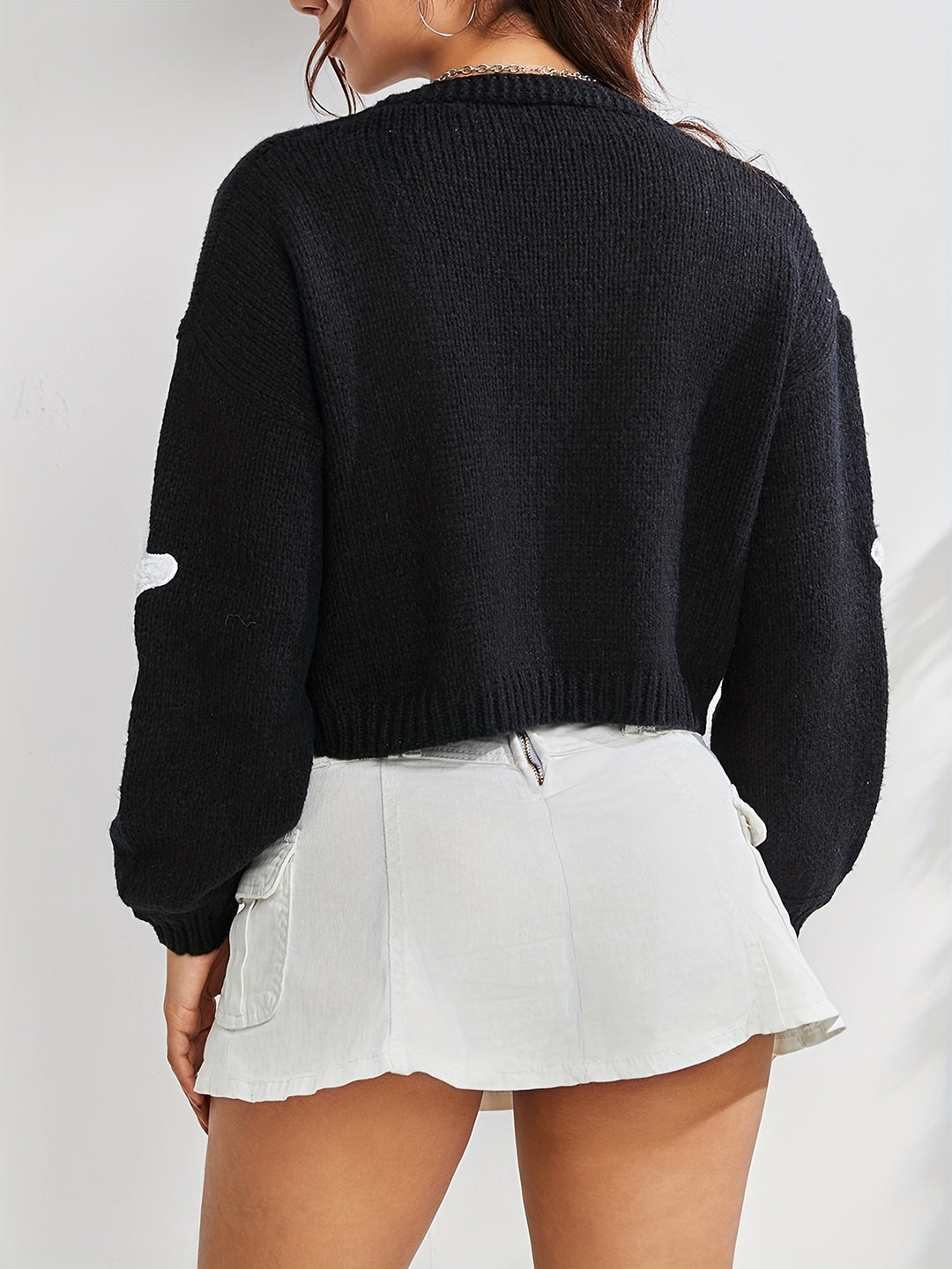 Back view of a cropped black knit cardigan with balloon sleeves, worn with a white skirt