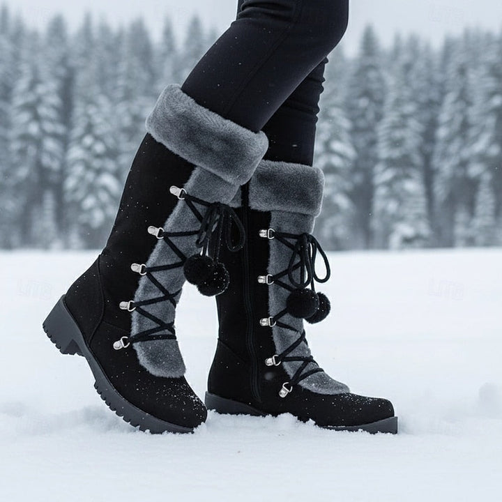 Black mid calf boots with a grey fur cuff, worn in the snow
