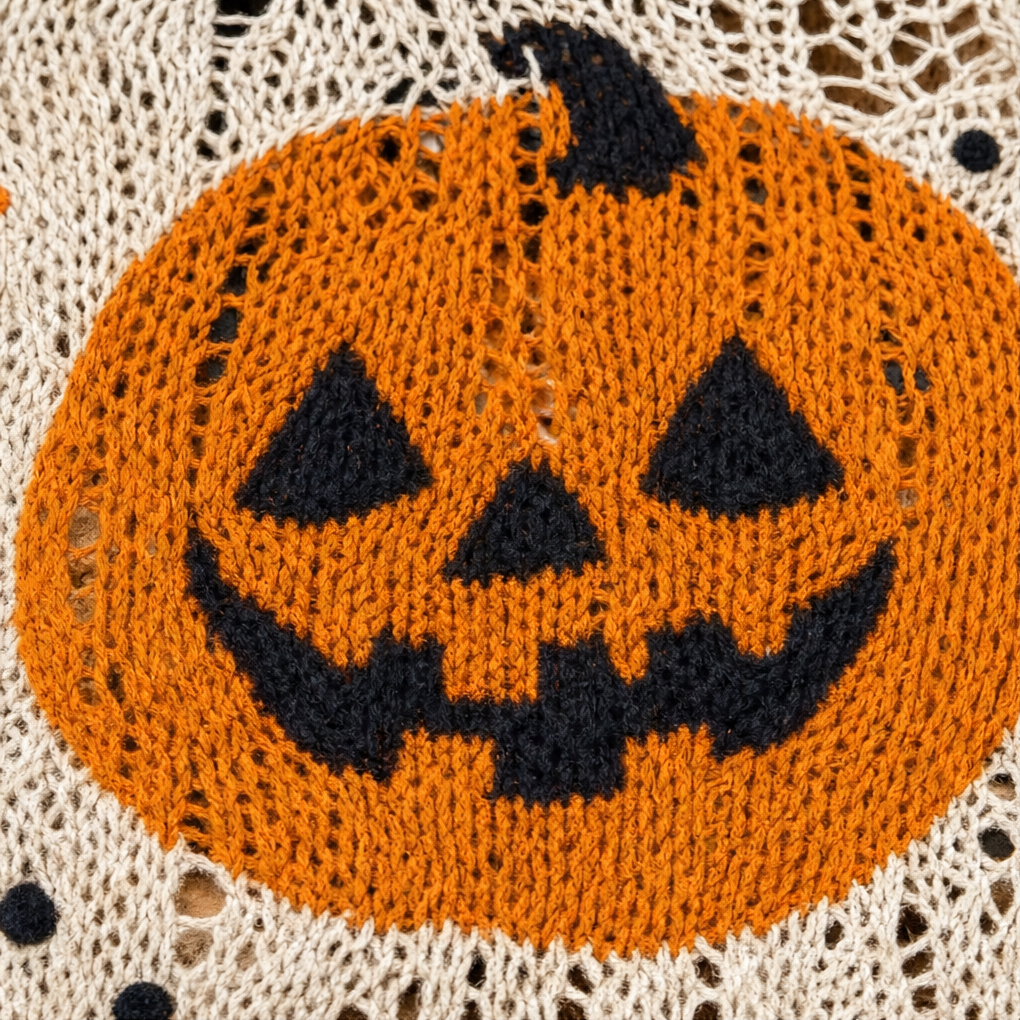 Close-up of an orange jack o lantern motif knitted into cream open weave fabric