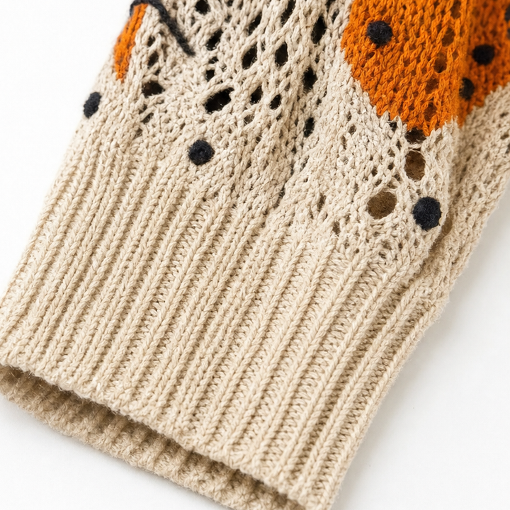 Close up of a beige open knit cuff with orange and black pattern detail above the ribbing