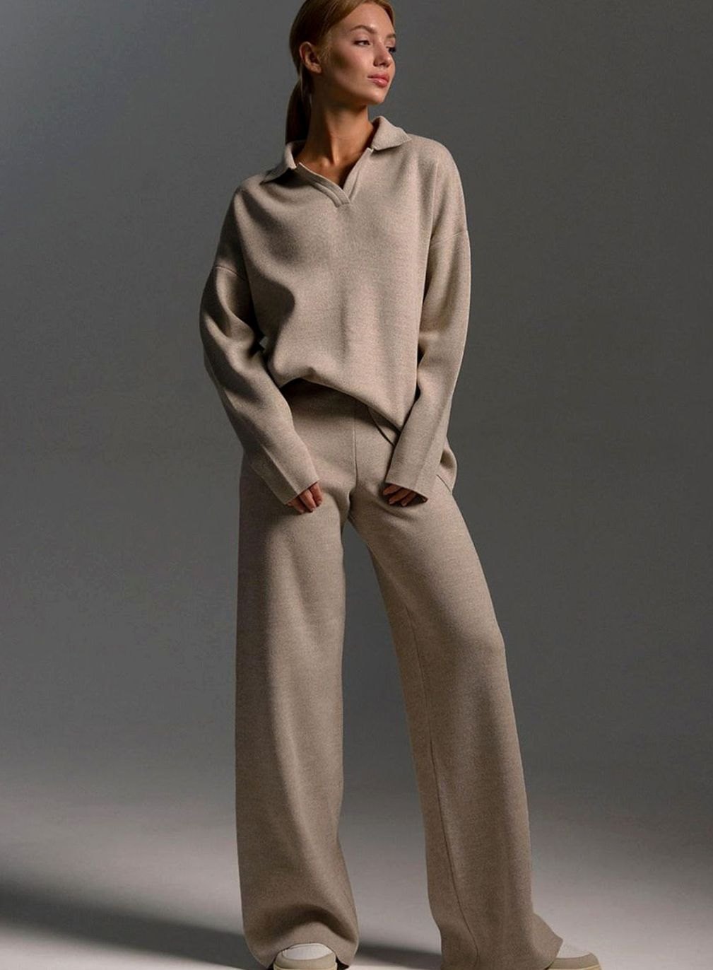 Woman wearing a beige two piece lounge set with a collared knit top and wide leg trousers, full length