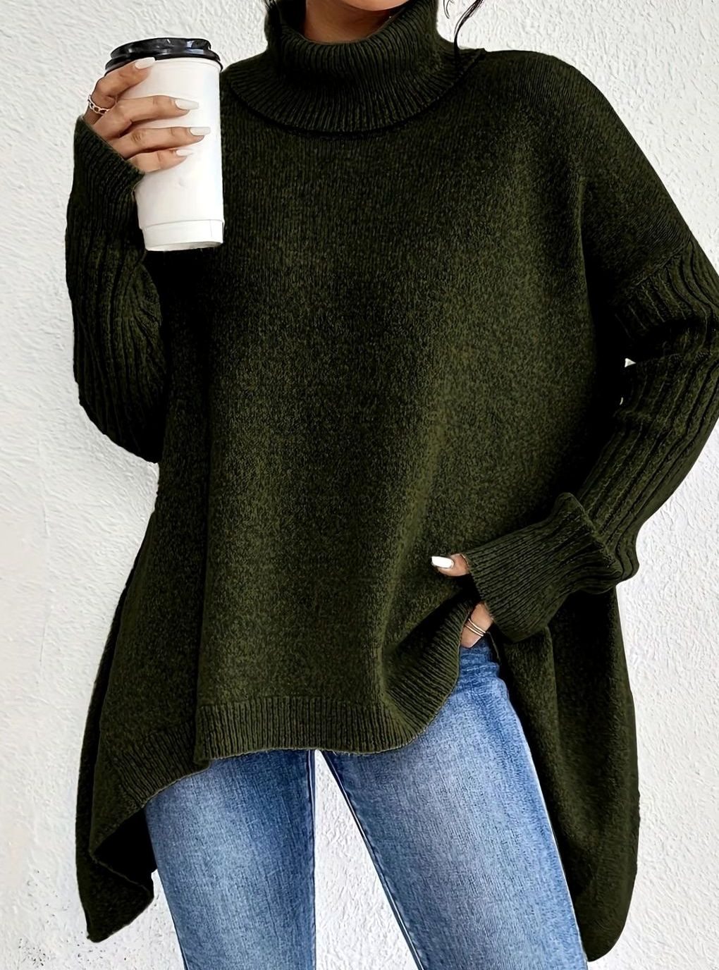 Woman in an oversized olive green turtleneck sweater with a longline hem, worn over blue jeans