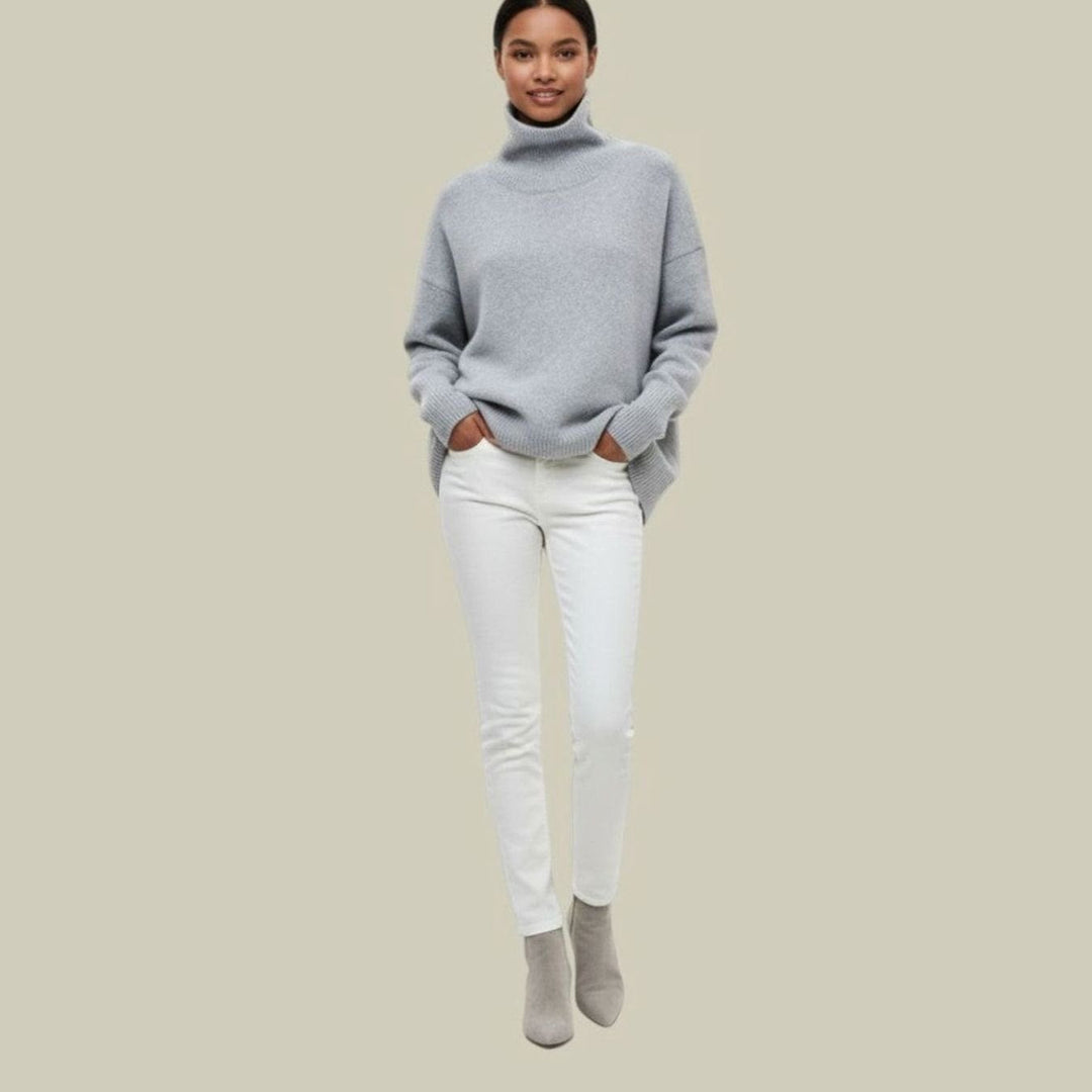 Full length view of a woman in a light grey oversized turtleneck sweater with white jeans