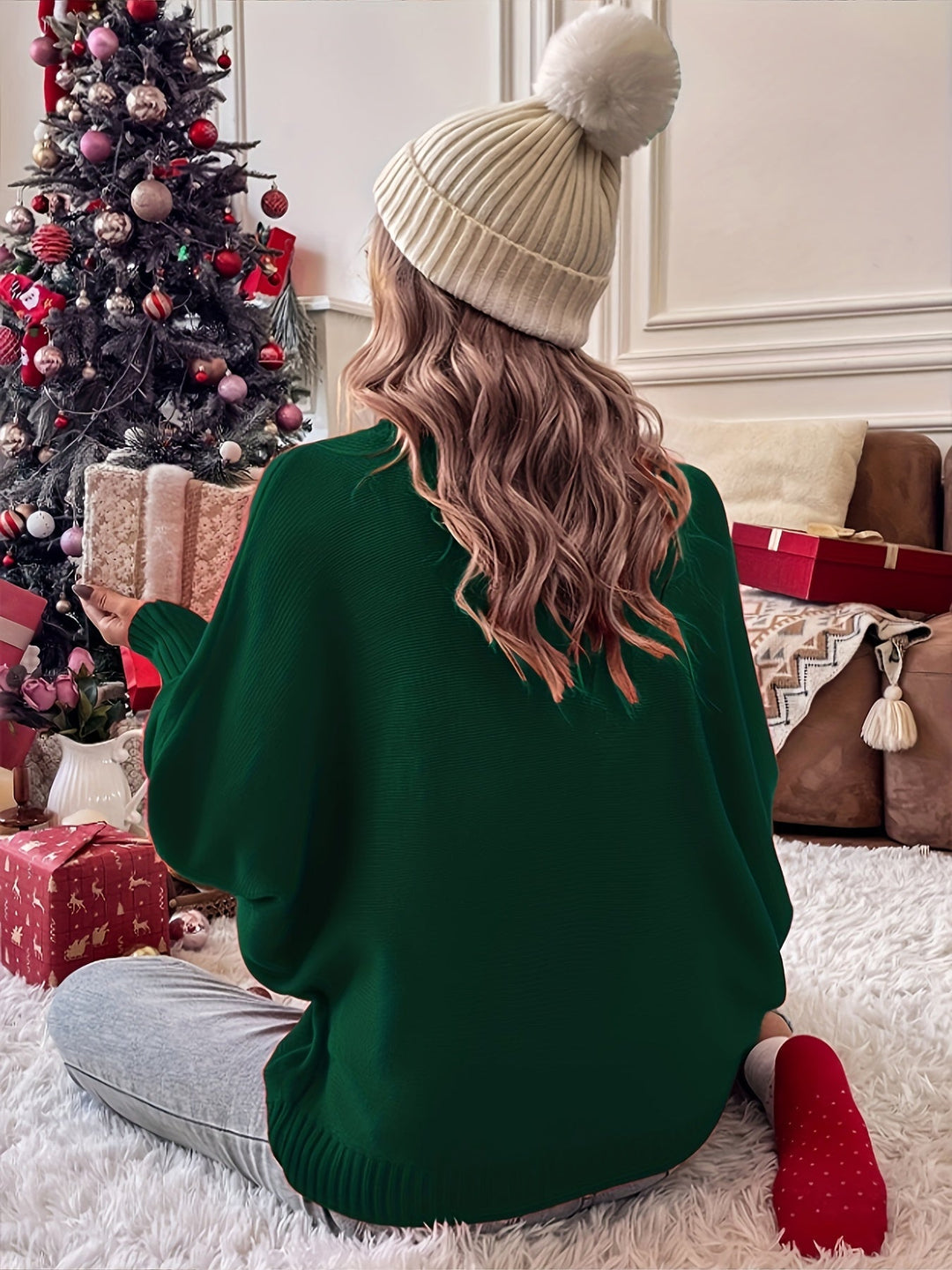 Back view of a green batwing sleeve sweater with a ribbed hem, worn seated