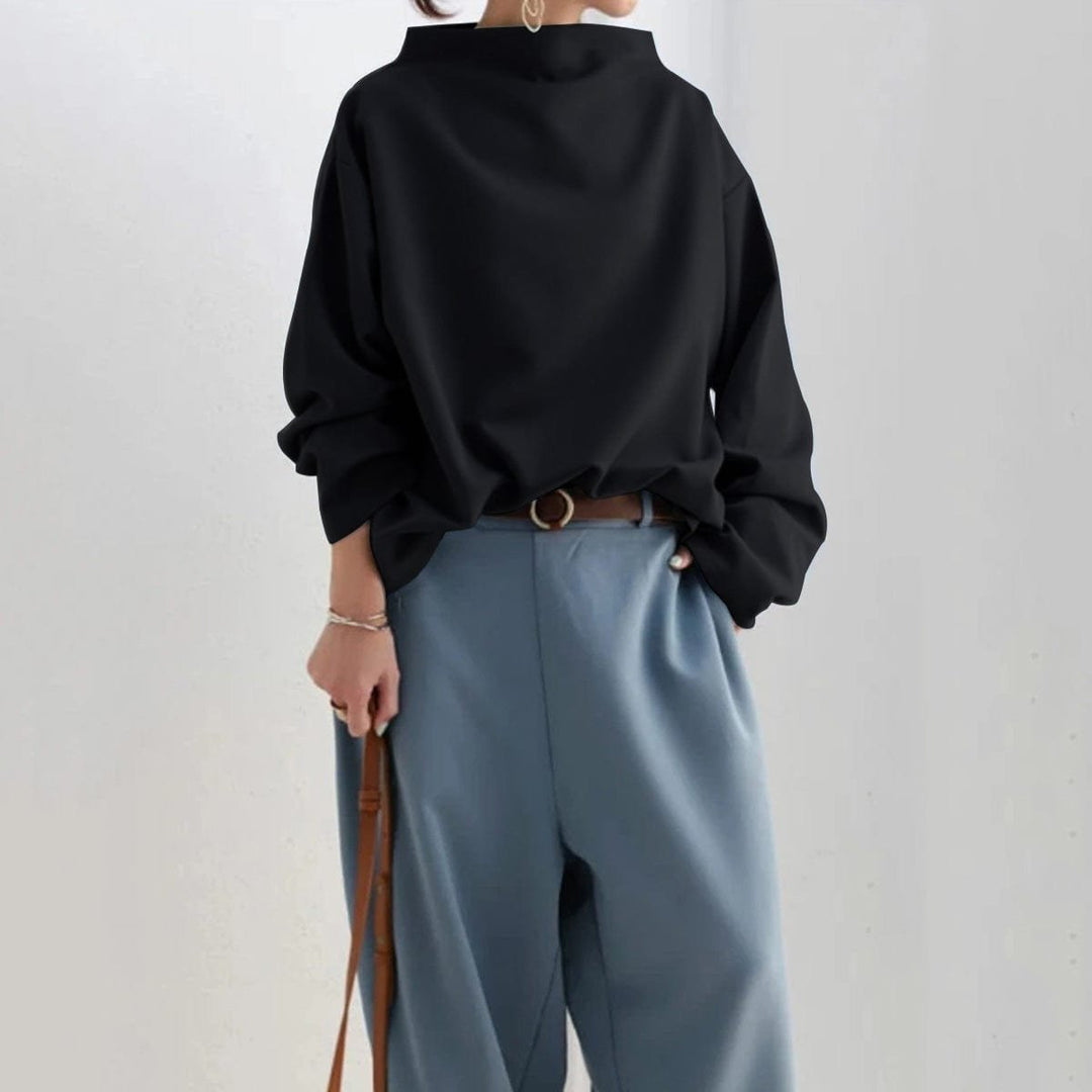 Black funnel neck dolman top tucked into blue grey pants, full front view