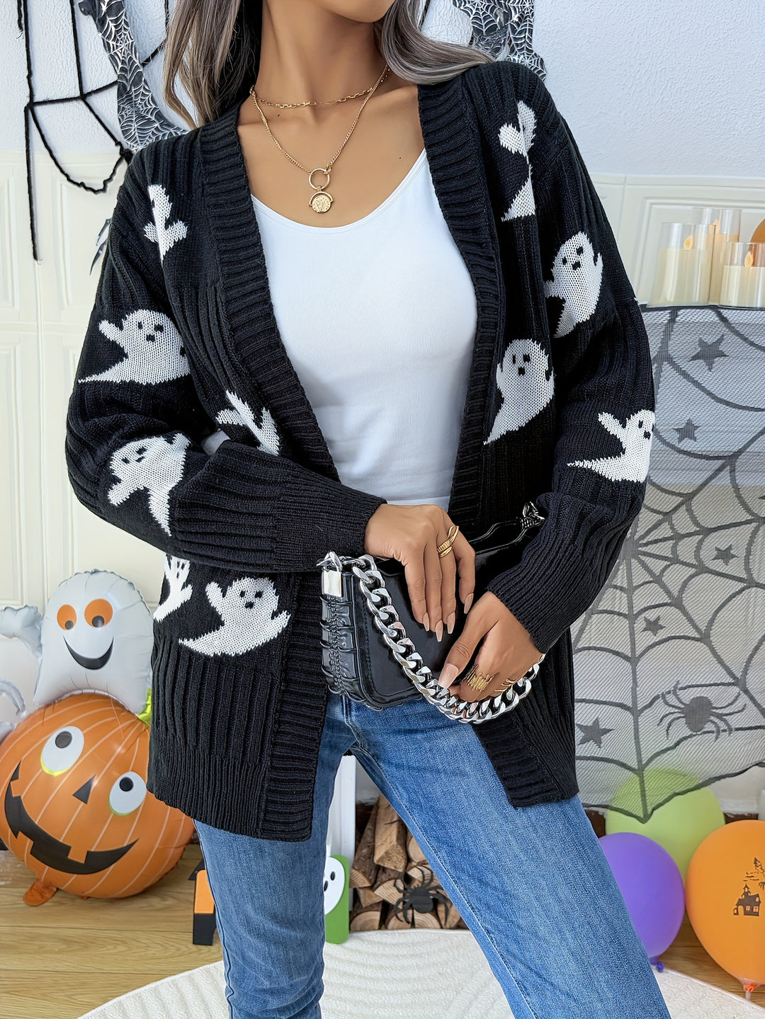Black knit cardigan with white ghost motifs, open front and drop shoulders, worn with jeans