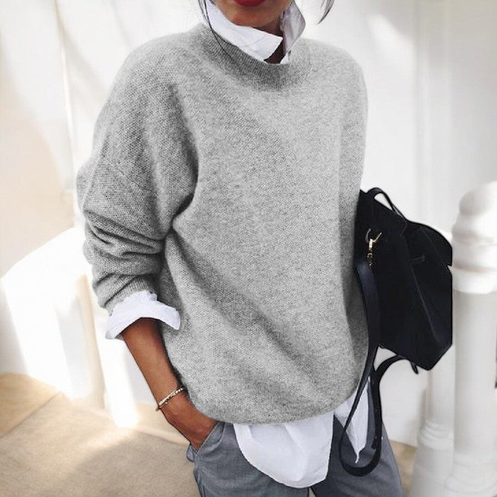 Woman in a light grey drop shoulder knit sweater layered over a white shirt