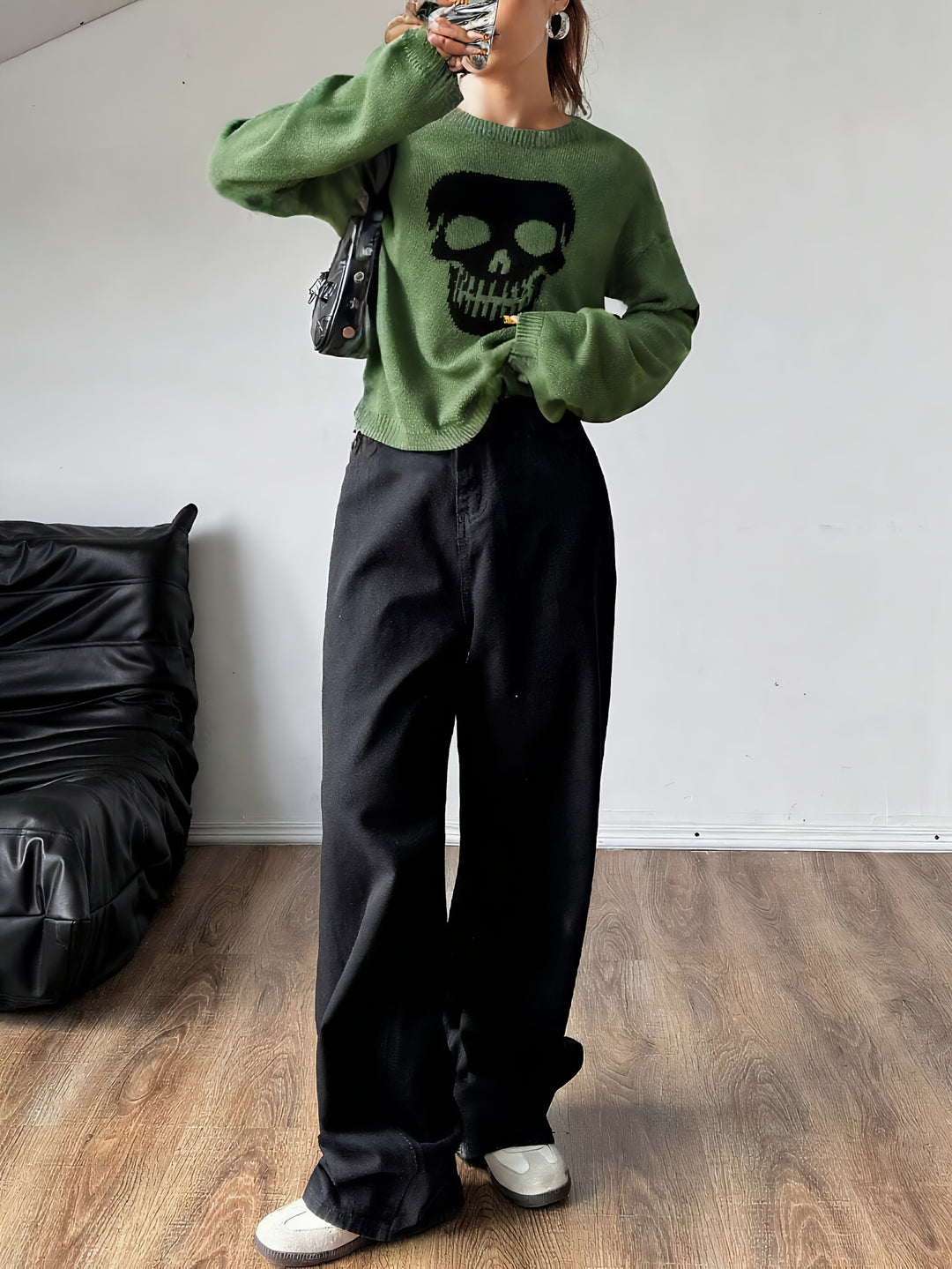 Green knit sweater with a black skull motif, worn with black wide leg trousers