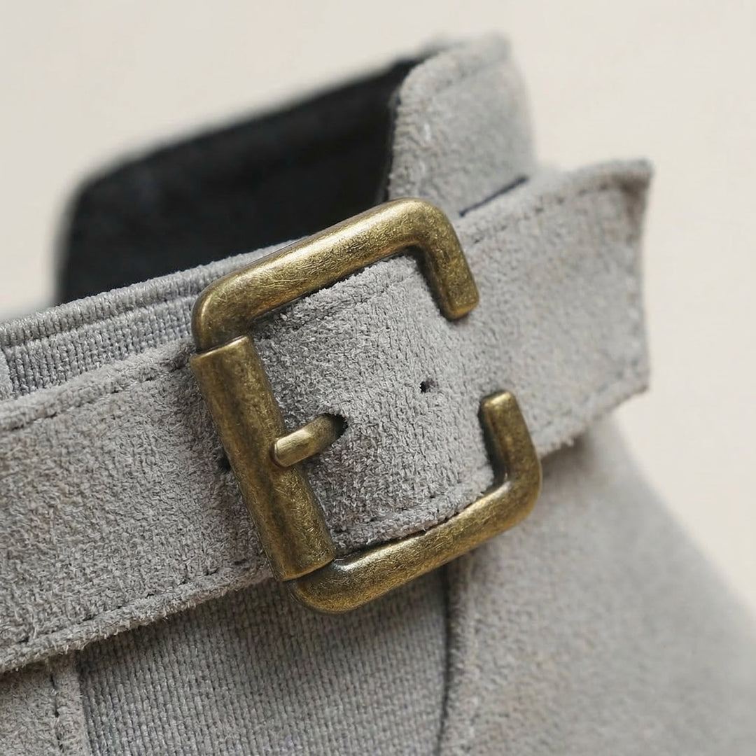 Close up of the antique gold buckle strap on a grey suede ankle boot