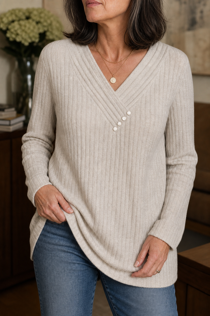 Close-up of an oatmeal ribbed V neck sweater with pearl buttons worn with blue jeans