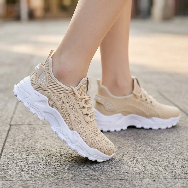 Beige knit sneakers with white chunky soles worn outdoors on a paved street