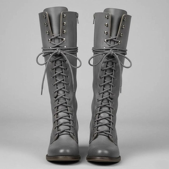Pair of grey lace up knee high boots with a studded shaft, shown from the front