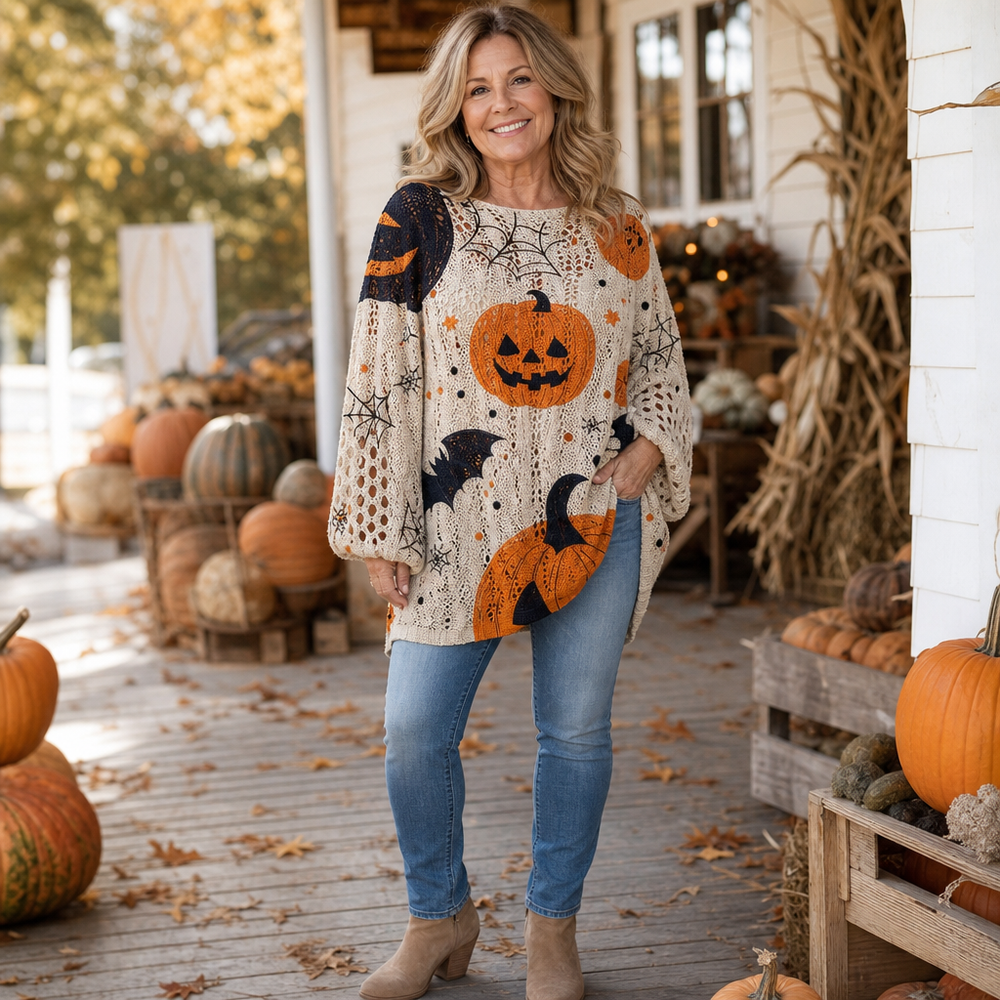 Cream open-knit sweater with orange pumpkin and black bat motifs, worn with jeans on a porch