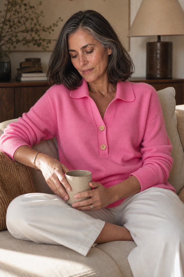 Woman in the pink polo collar sweater with wooden buttons, seated with a mug