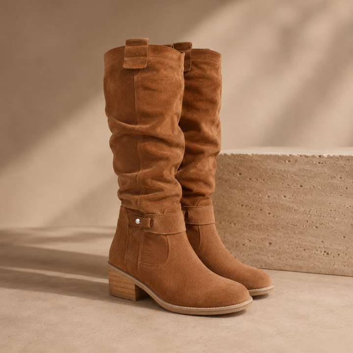 Tan suede knee high boots with a slouched shaft and ankle strap
