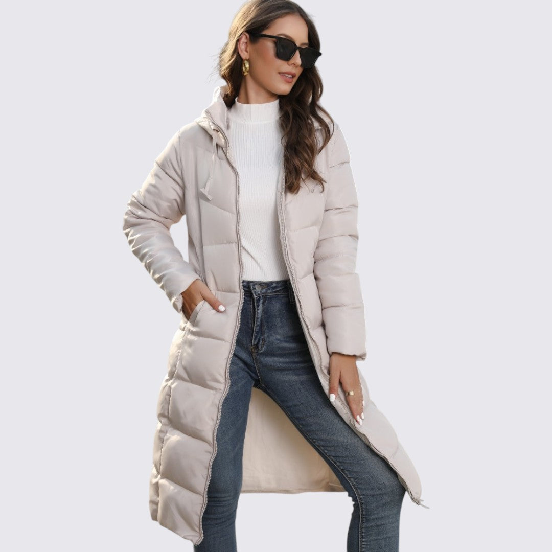 Woman in a beige long quilted hooded puffer coat worn open over jeans and a white top