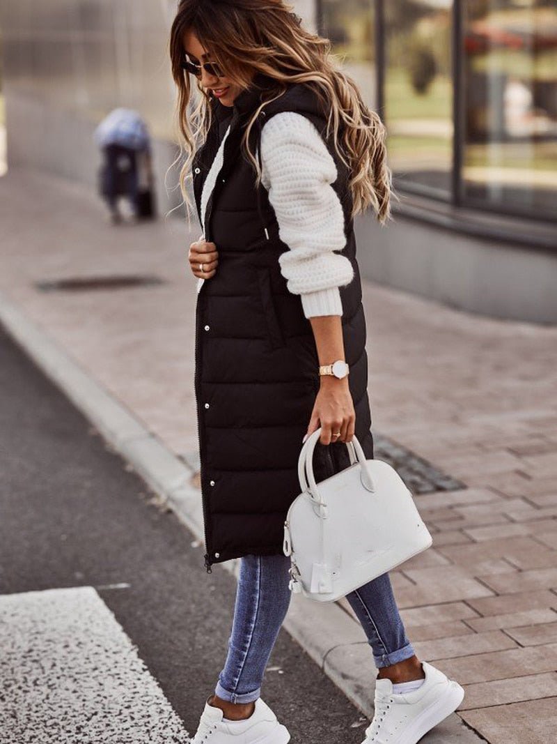 Black longline hooded puffer vest worn over a white knit, side view