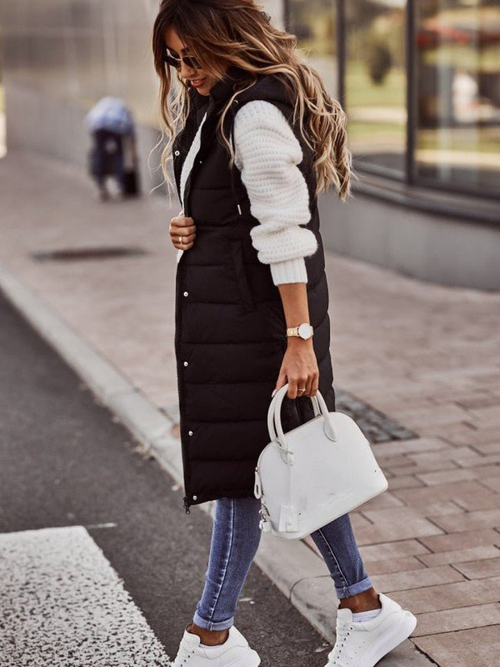 Black longline hooded puffer vest worn over a white knit, side view