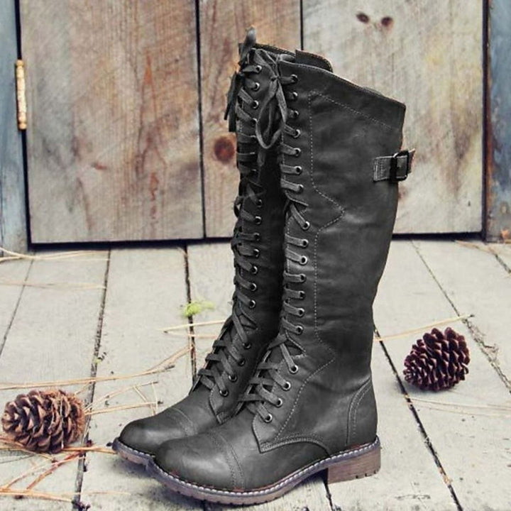 Pair of charcoal grey tall lace-up riding boots standing on weathered wood