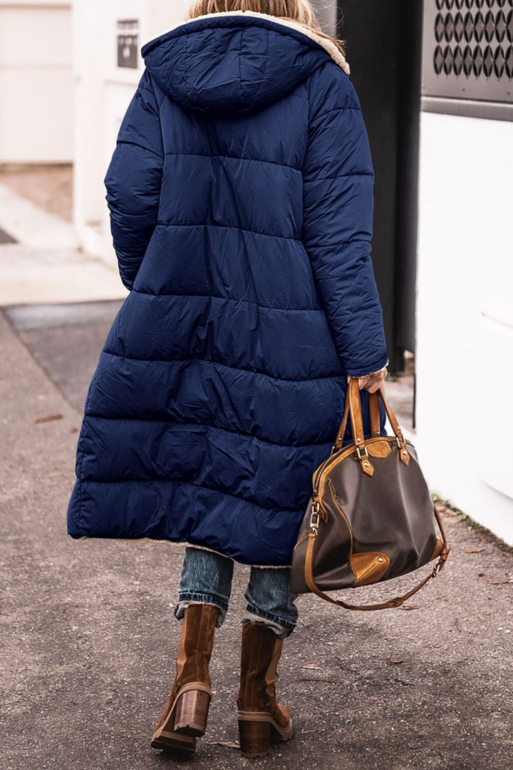 Back view of a woman in a long navy quilted hooded coat with a cream sherpa collar and hem