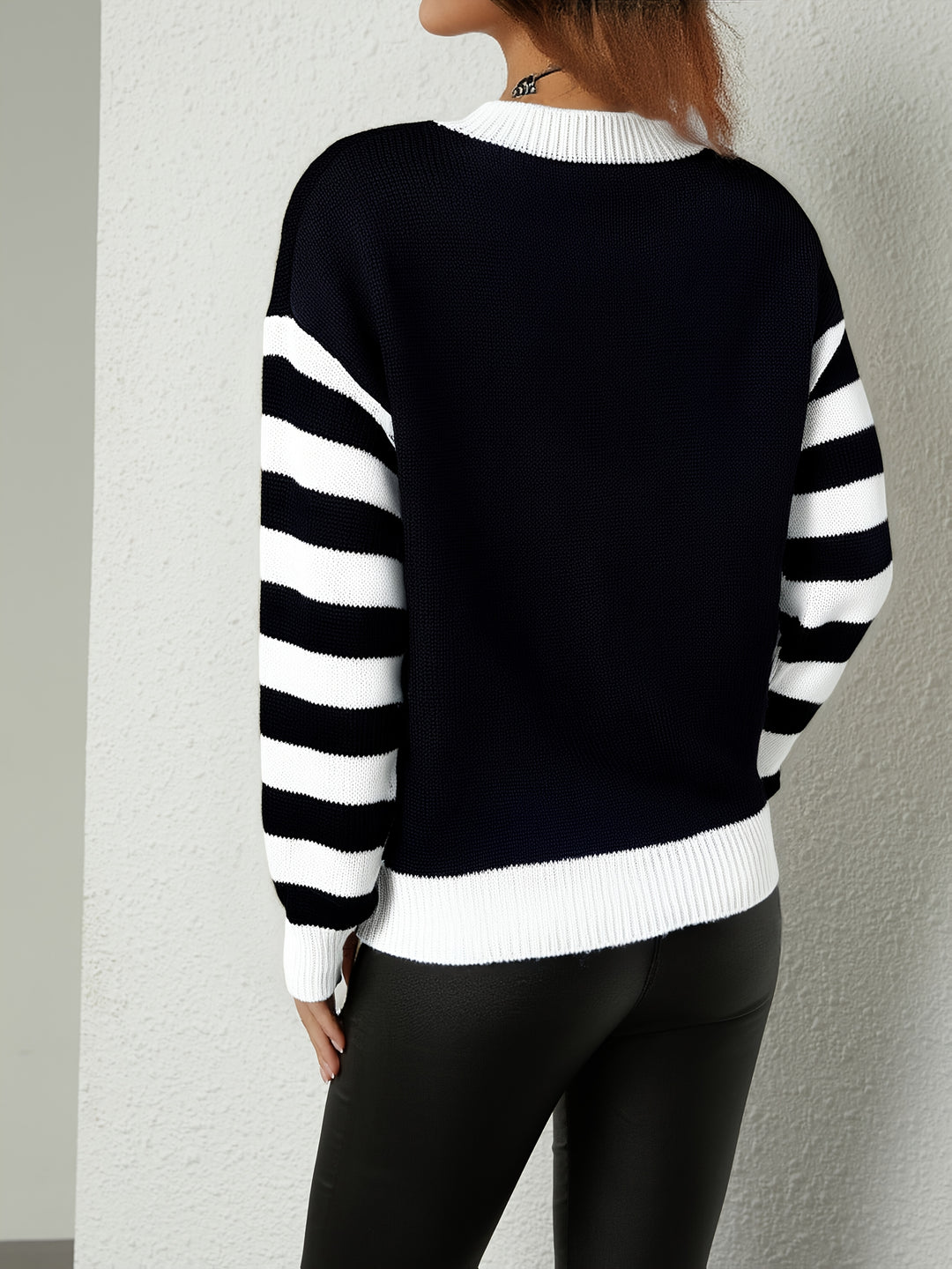 Back view of a navy knit sweater with black and white striped sleeves and white ribbed trim