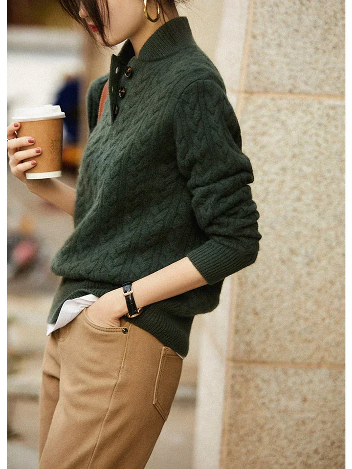 Olive green cable knit sweater with a stand collar, worn outdoors holding a coffee cup