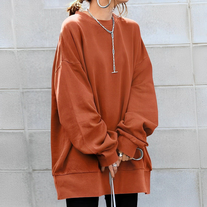 Rust oversized crew neck sweatshirt worn against a concrete wall, front view