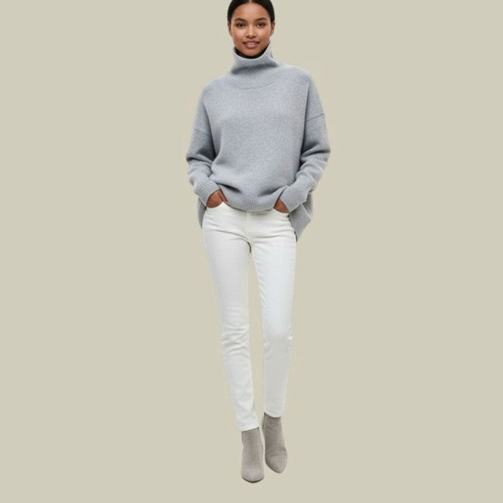 Full length view of a woman in a light grey oversized turtleneck sweater with white jeans