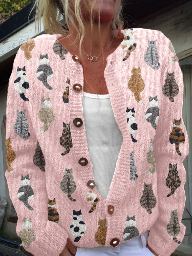 Pink knit cardigan covered in cat motifs, button front, worn open over a white top