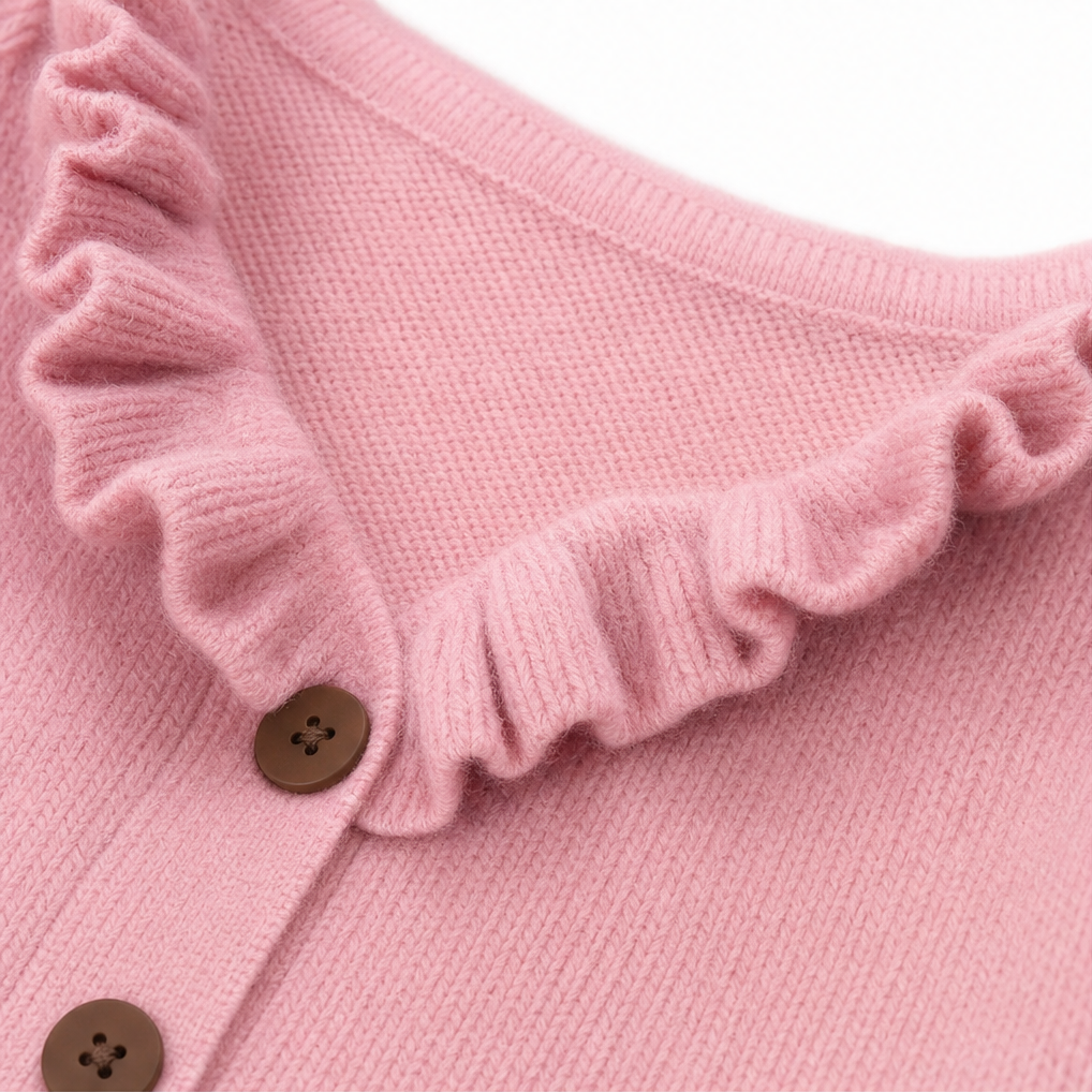 Close-up of a pink knit cardigan showing the ruffle trimmed neckline and brown buttons