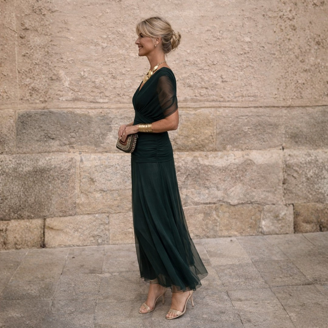 Dark green pleated wrap midi dress, side view with a clutch
