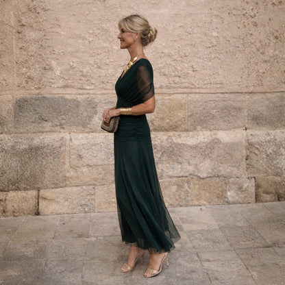 Dark green pleated wrap midi dress, side view with a clutch