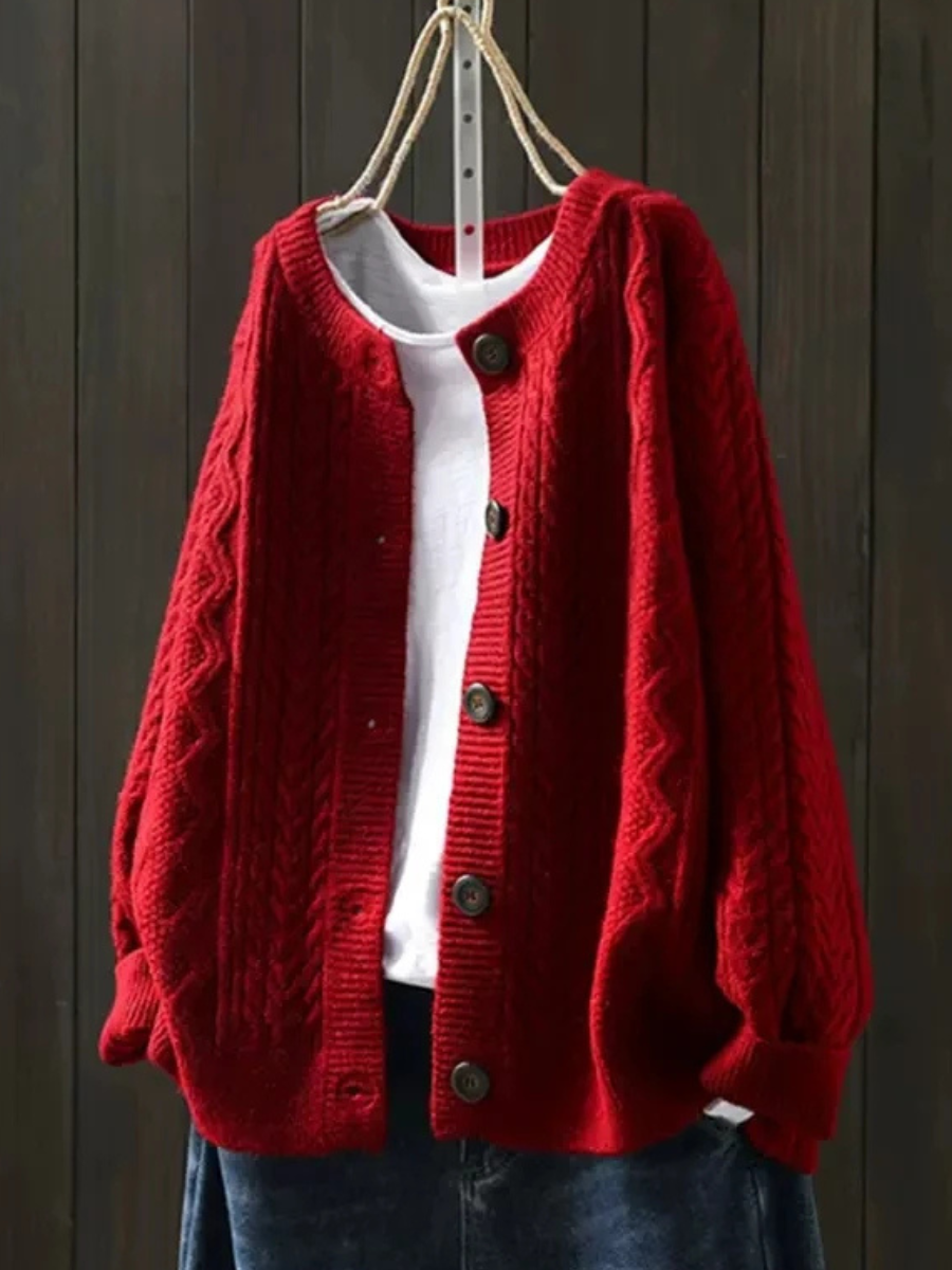Red cable knit cardigan with dark buttons hanging on a wooden wall