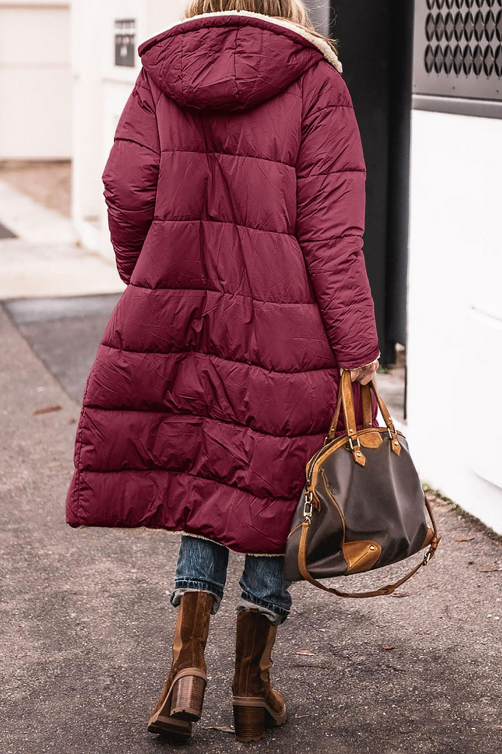 Back view of the burgundy longline padded coat worn outdoors with boots