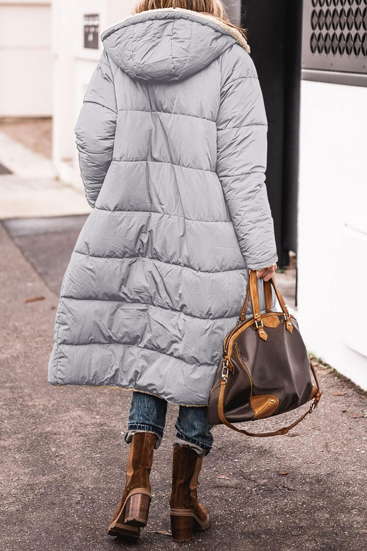 Back view of a light grey longline padded coat with a hood and cream lining on a street