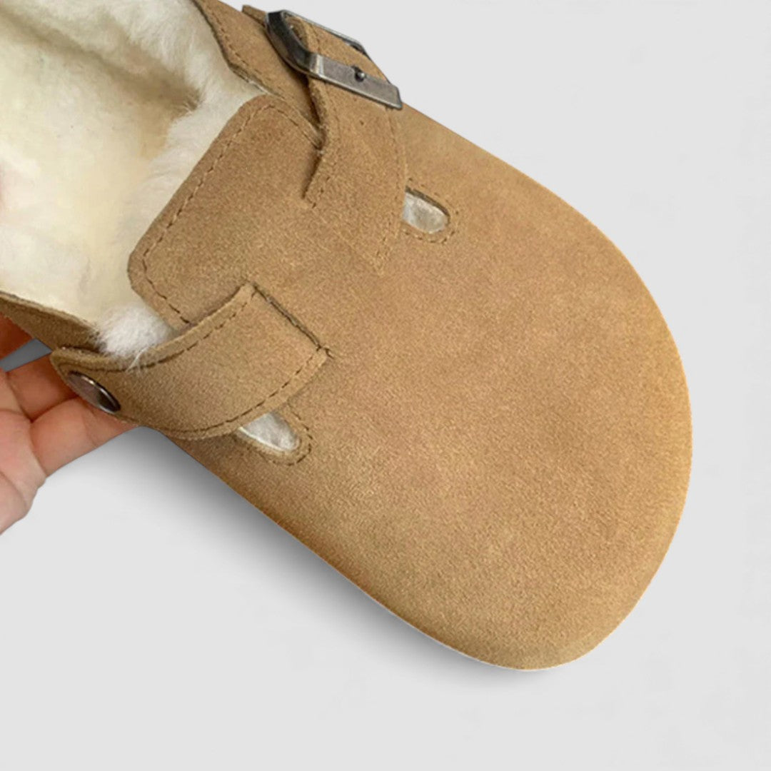 Close up of a tan suede clog with cream shearling lining and a metal buckle strap