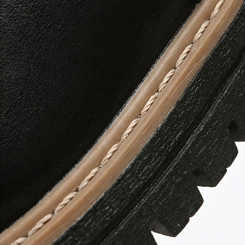 Close-up of a black ankle boot showing the contrast stitched welt and lugged platform sole
