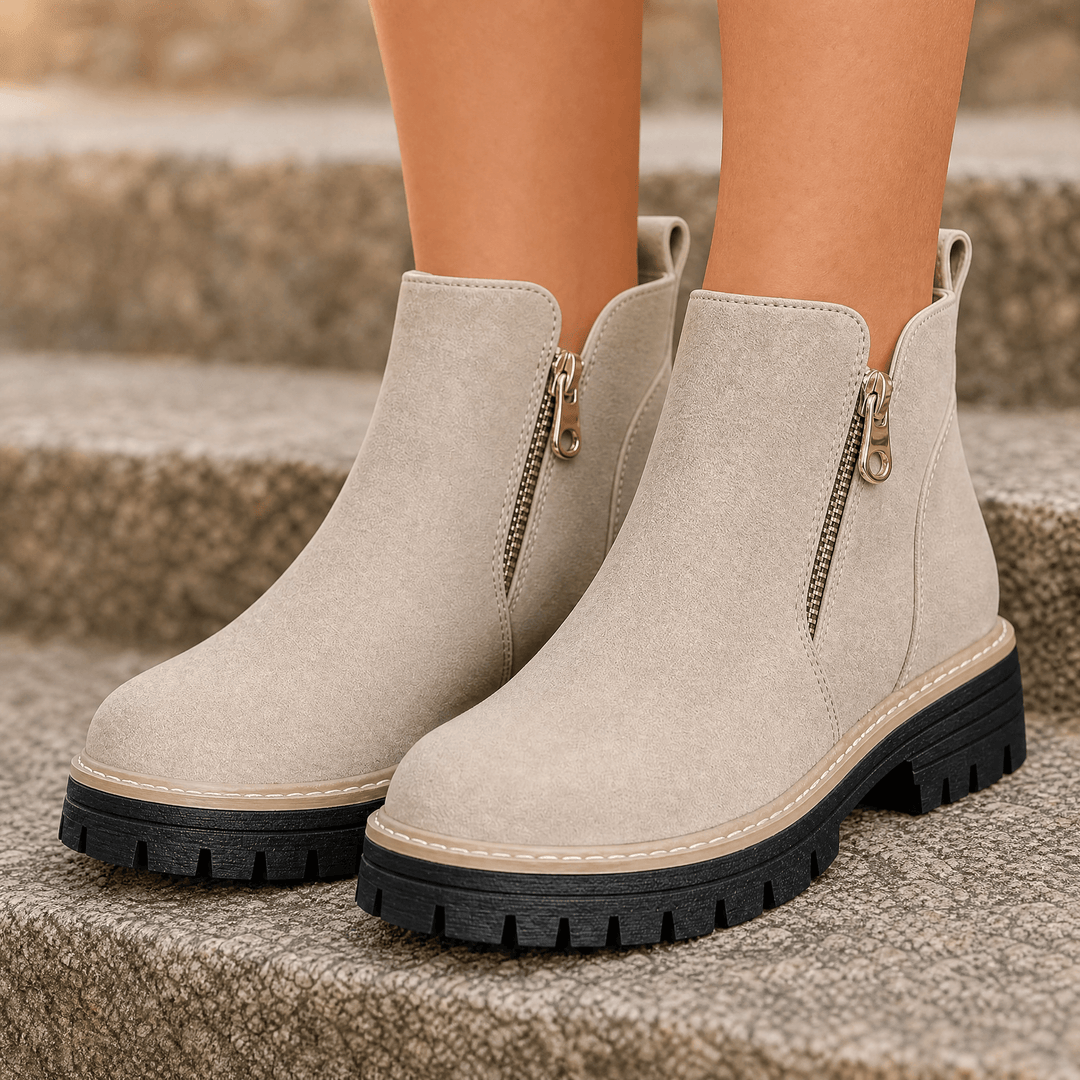 Beige suede platform ankle boots with side zips and chunky lug soles, worn on stone steps
