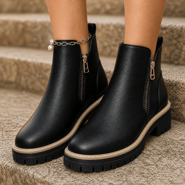 Black platform ankle boots with gold side zip and chain detail, worn on stone steps